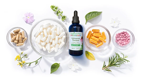 Various colours of supplement tablets in glass bowls on a white background surrounded by herbs and flowers, there is a small blue Supplement Place Echinacea Tincture bottle in the centre